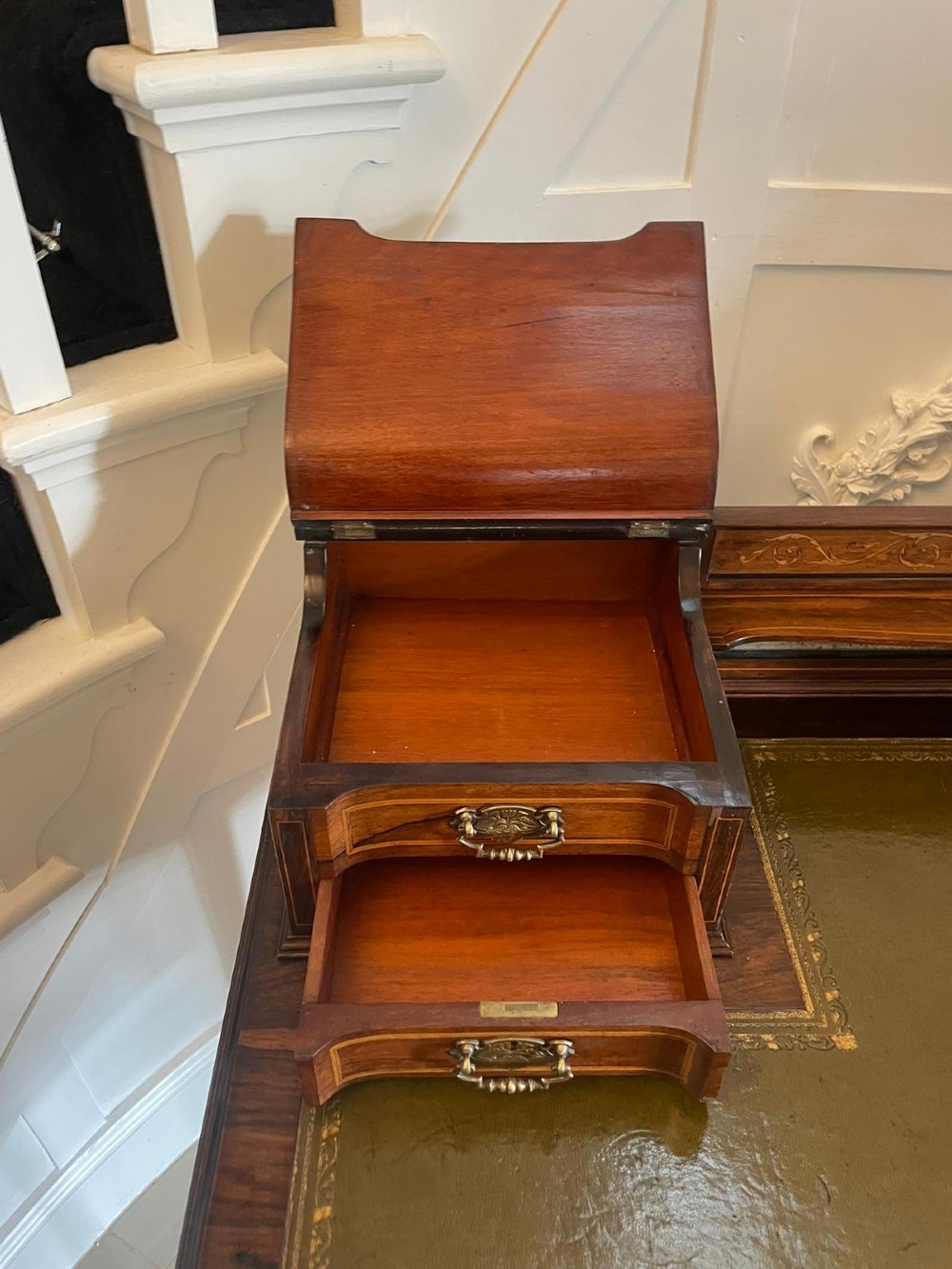 An antique Victorian inlaid writing desk with a green leather top, brass gallery railing, and multiple drawers on tapered legs with castors. View VI
