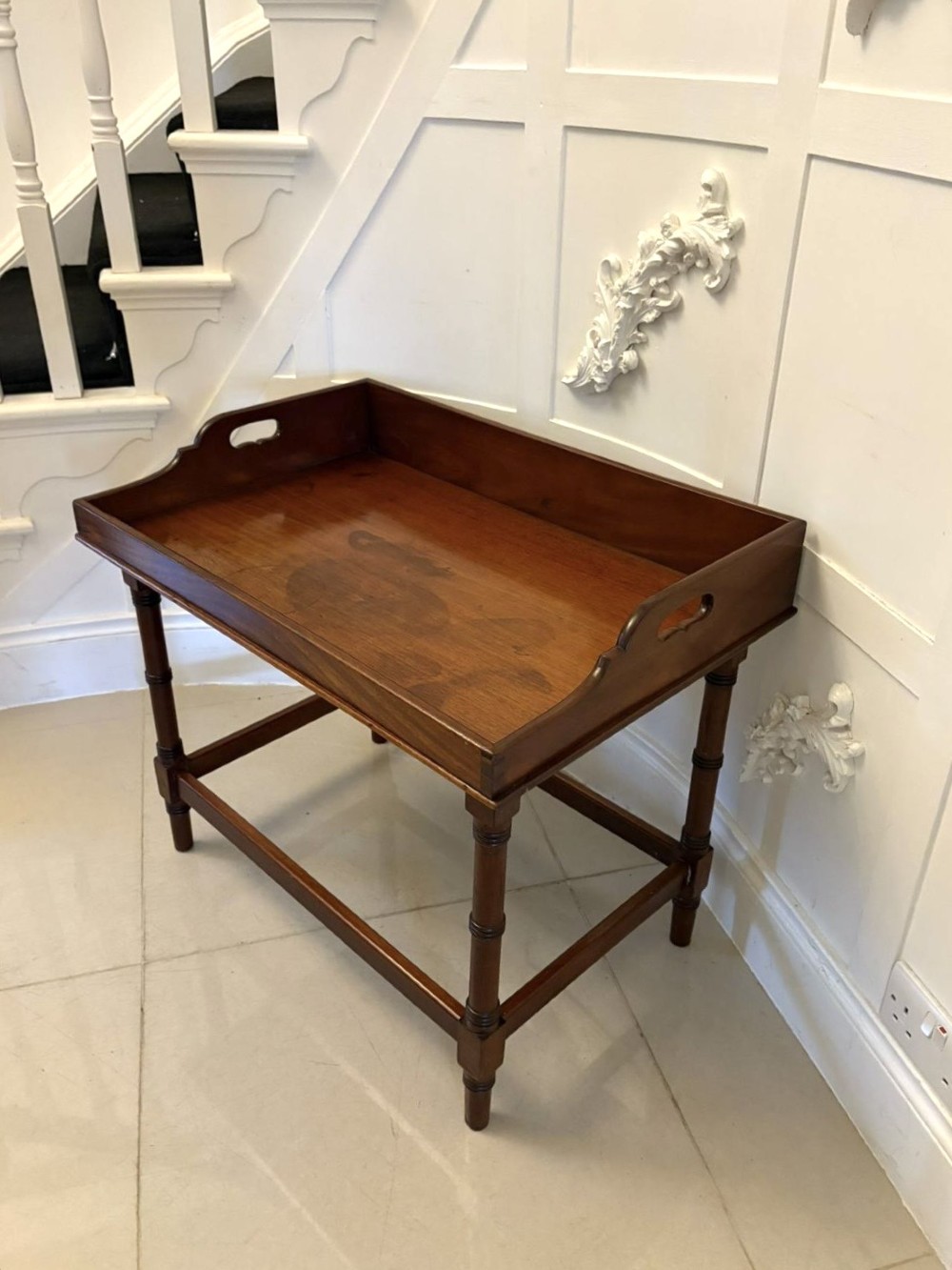 A dark mahogany tray-top occasional table featuring a raised gallery with carved carrying handles, turned legs, and stretchers.