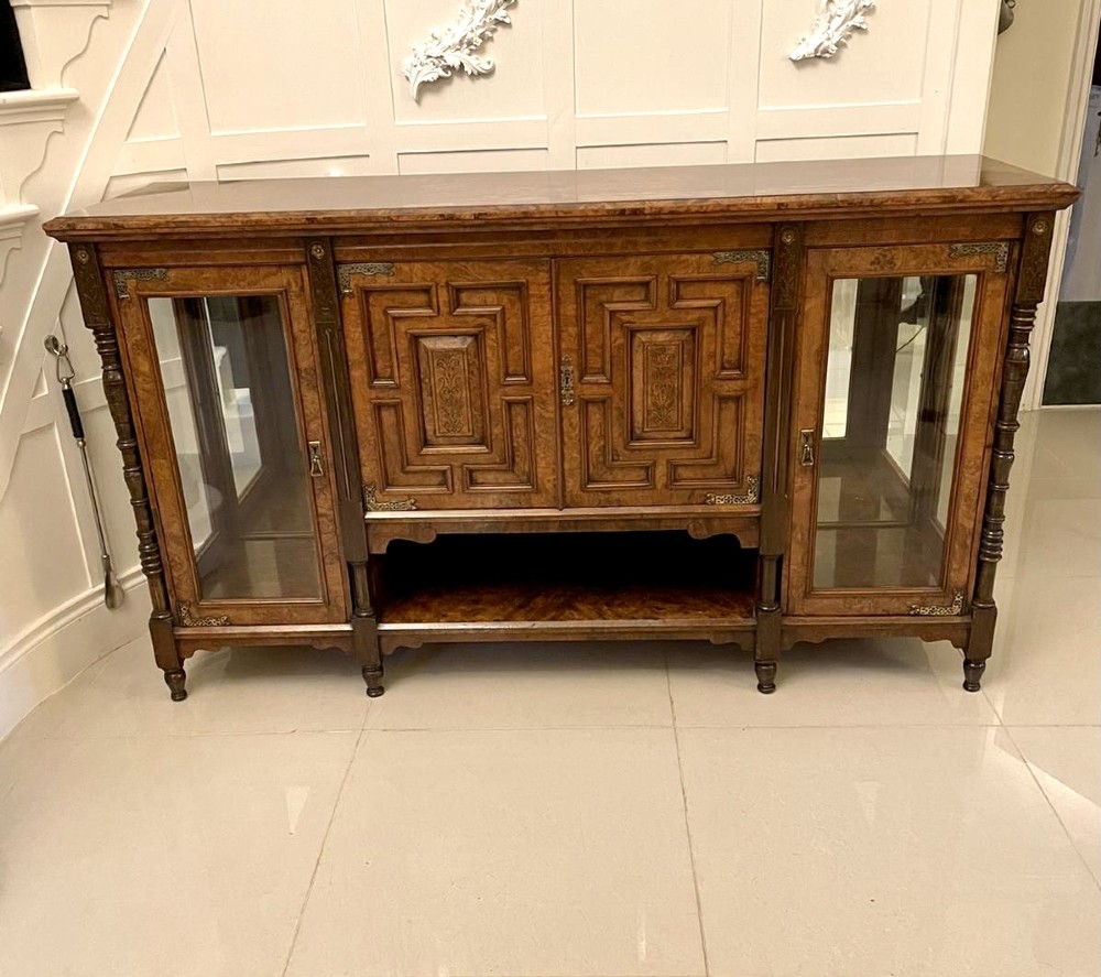 An antique Victorian burr walnut credenza featuring glazed flank doors, central geometric inlaid doors, brass fittings, and turned support columns.