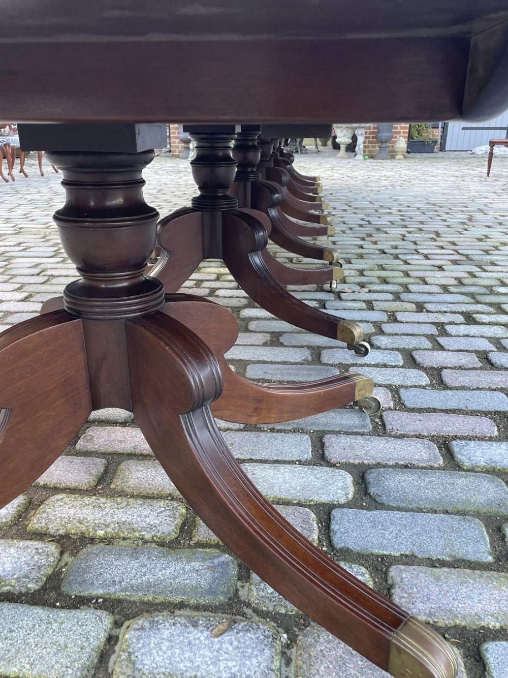 A long George III mahogany extending dining table with multiple pedestal bases resting on splayed reeded legs with brass castors. View II
