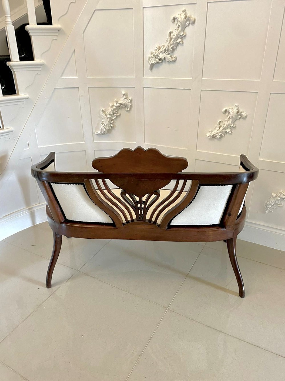An antique Victorian mahogany settee featuring cream upholstered seating, curved arms, cabriole legs, and a central back splat with intricate floral wood inlay. View VII
