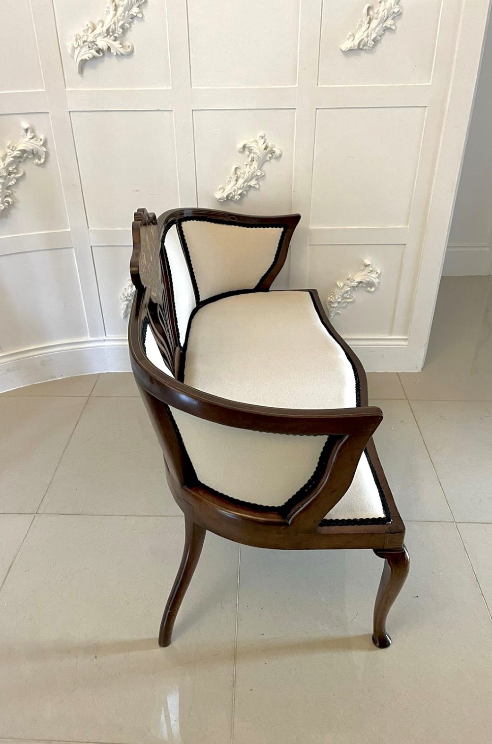 An antique Victorian mahogany settee featuring cream upholstered seating, curved arms, cabriole legs, and a central back splat with intricate floral wood inlay. View VIII