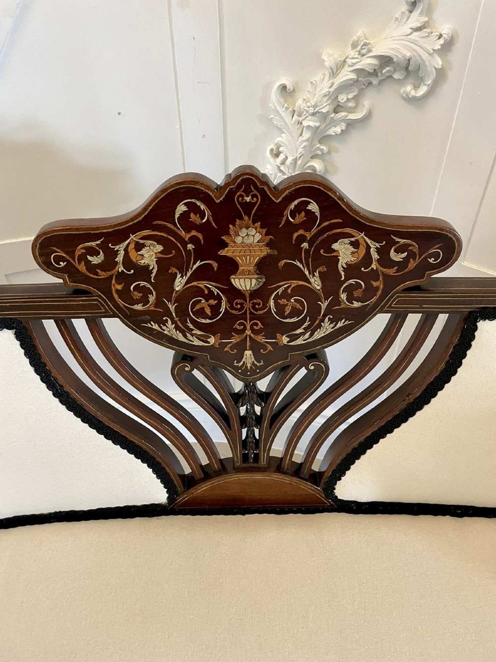 An antique Victorian mahogany settee featuring cream upholstered seating, curved arms, cabriole legs, and a central back splat with intricate floral wood inlay. View IX