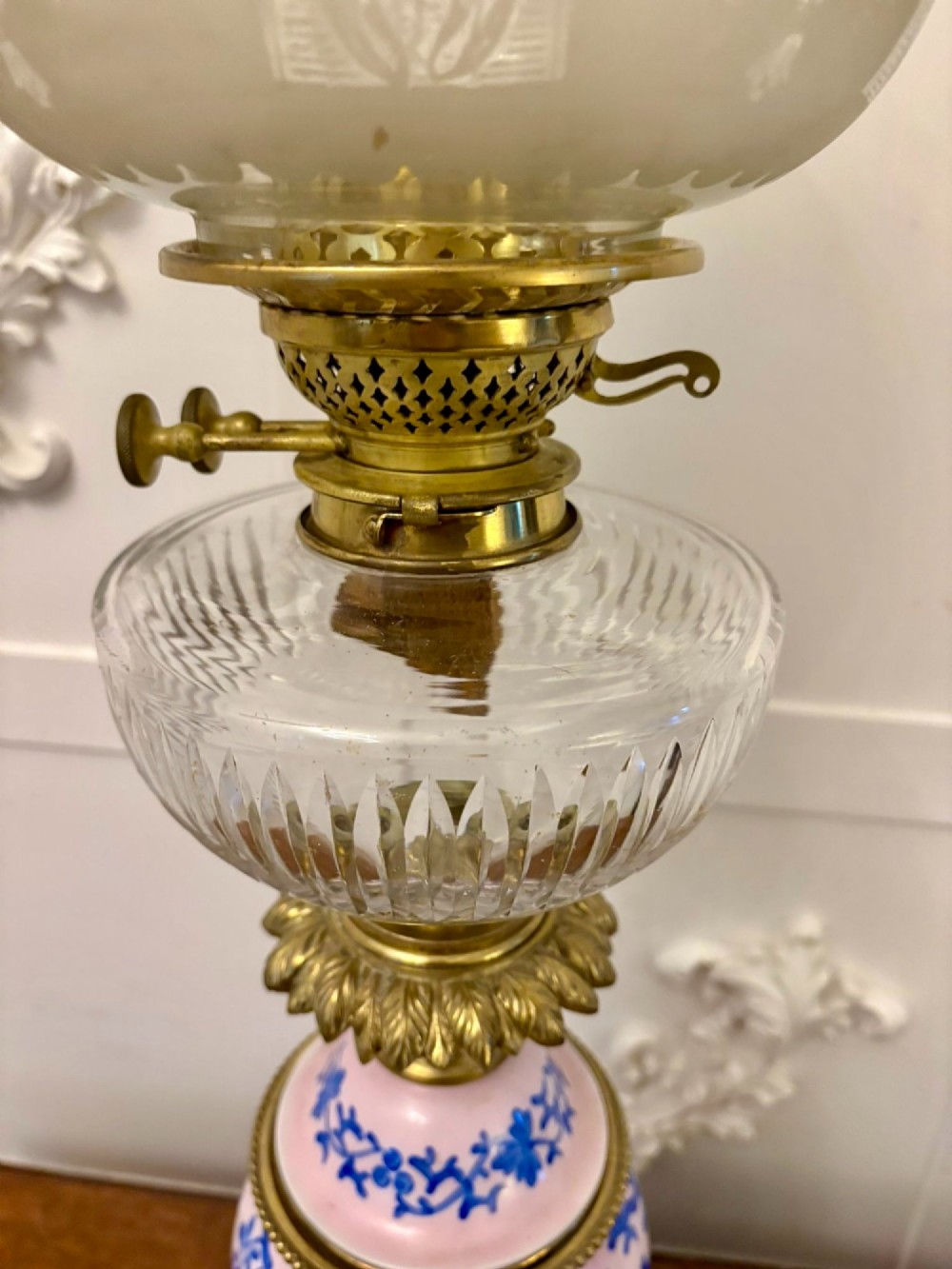 A tall Victorian oil lamp featuring a pink porcelain body with blue floral trellis decoration, a cast brass base, a cut glass reservoir, and an etched glass shade. View VI