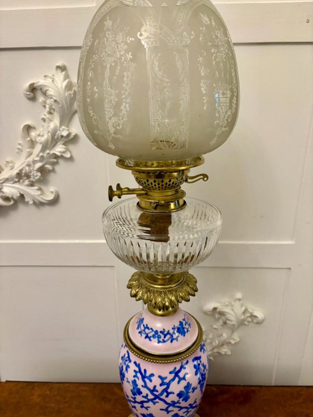 A tall Victorian oil lamp featuring a pink porcelain body with blue floral trellis decoration, a cast brass base, a cut glass reservoir, and an etched glass shade. View X