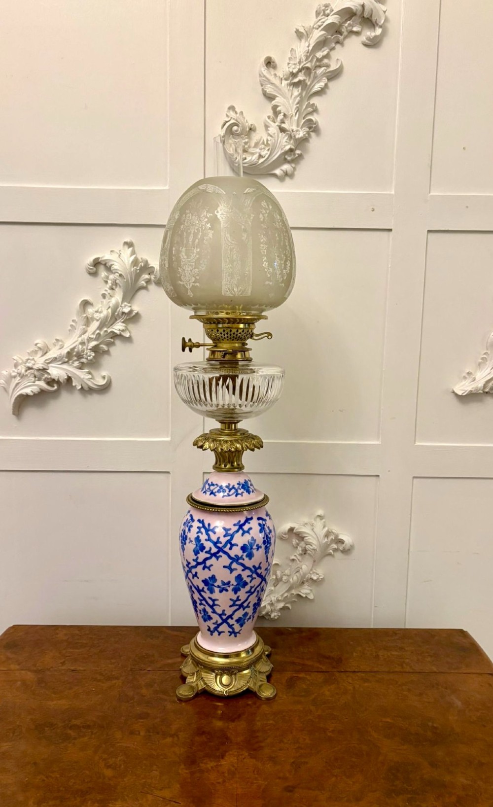 A tall Victorian oil lamp featuring a pink porcelain body with blue floral trellis decoration, a cast brass base, a cut glass reservoir, and an etched glass shade. View XIII