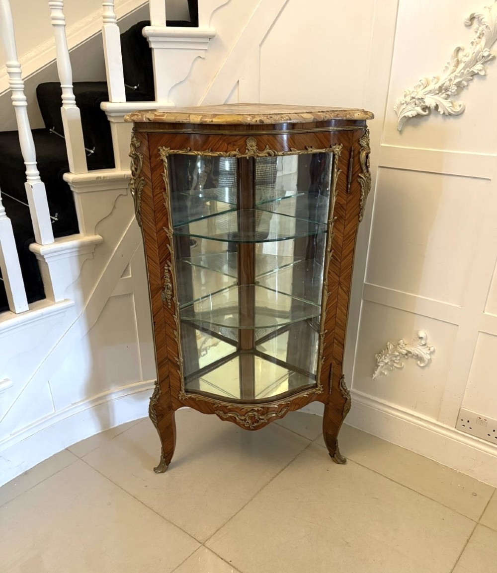 An antique French serpentine corner display cabinet crafted from kingwood with a marble top, curved glass door, internal glass shelves, and gilded ormolu mounts.