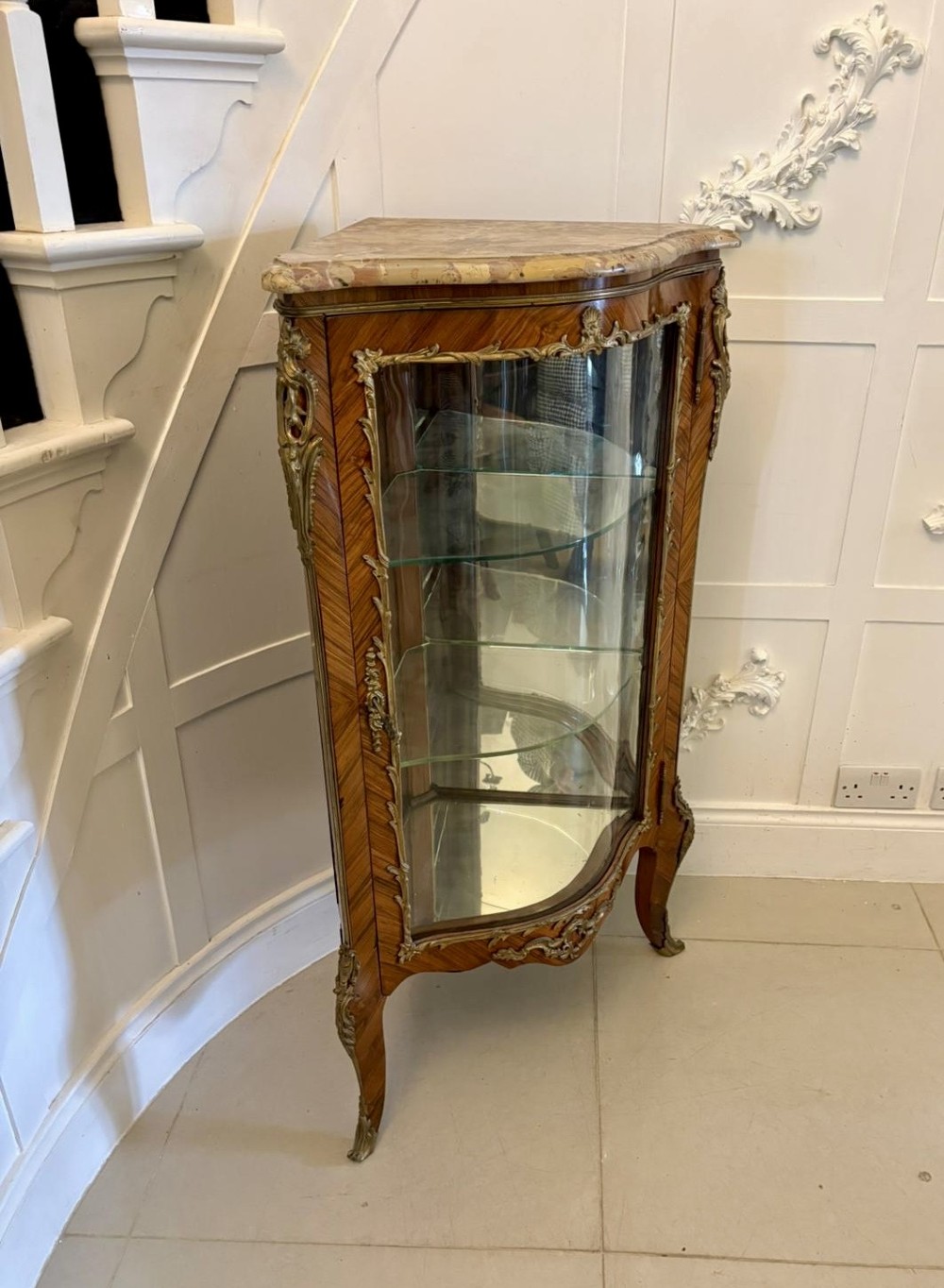 An antique French serpentine corner display cabinet crafted from kingwood with a marble top, curved glass door, internal glass shelves, and gilded ormolu mounts. View X