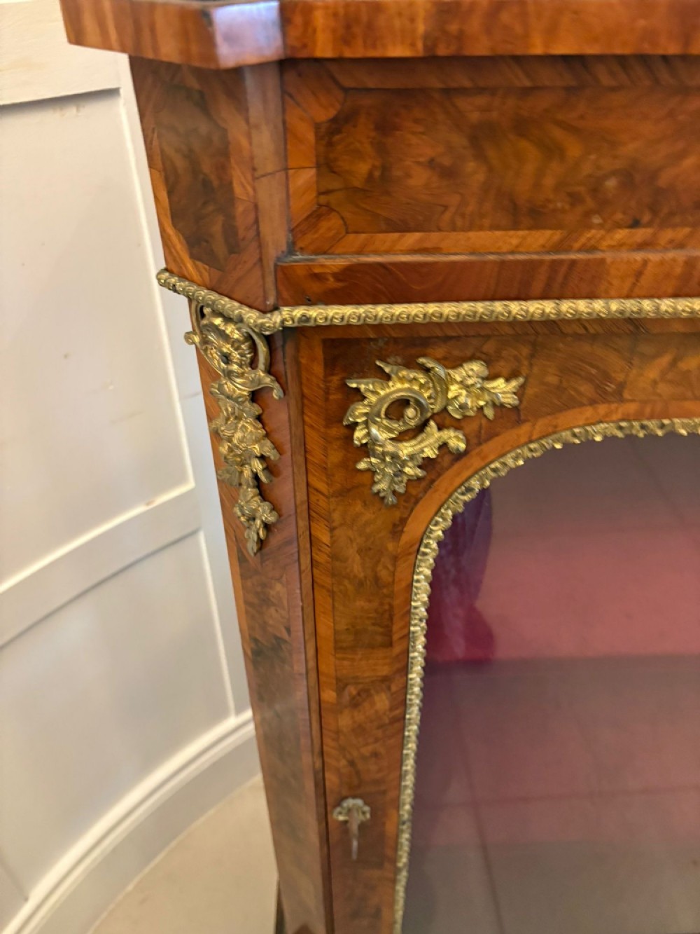 A pair of Victorian burr walnut pier cabinets featuring glazed front doors, velvet-lined interior shelves, and ornate gilt metal mounts. View V