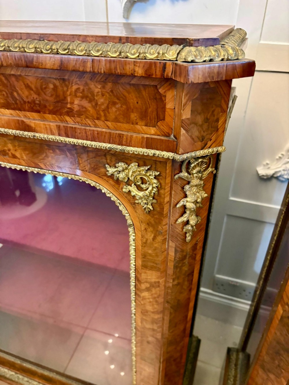 A pair of Victorian burr walnut pier cabinets featuring glazed front doors, velvet-lined interior shelves, and ornate gilt metal mounts. View VII