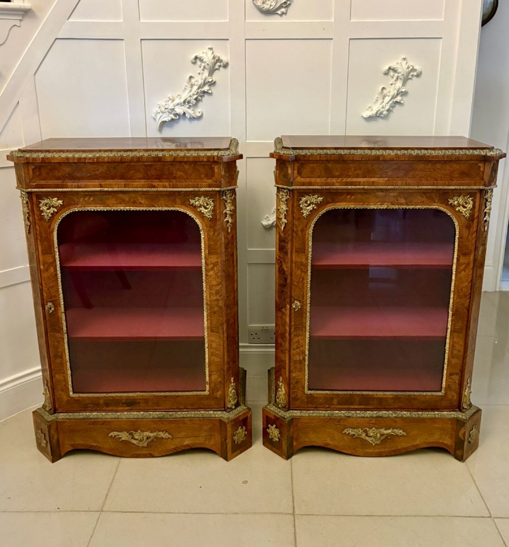 A pair of Victorian burr walnut pier cabinets featuring glazed front doors, velvet-lined interior shelves, and ornate gilt metal mounts.