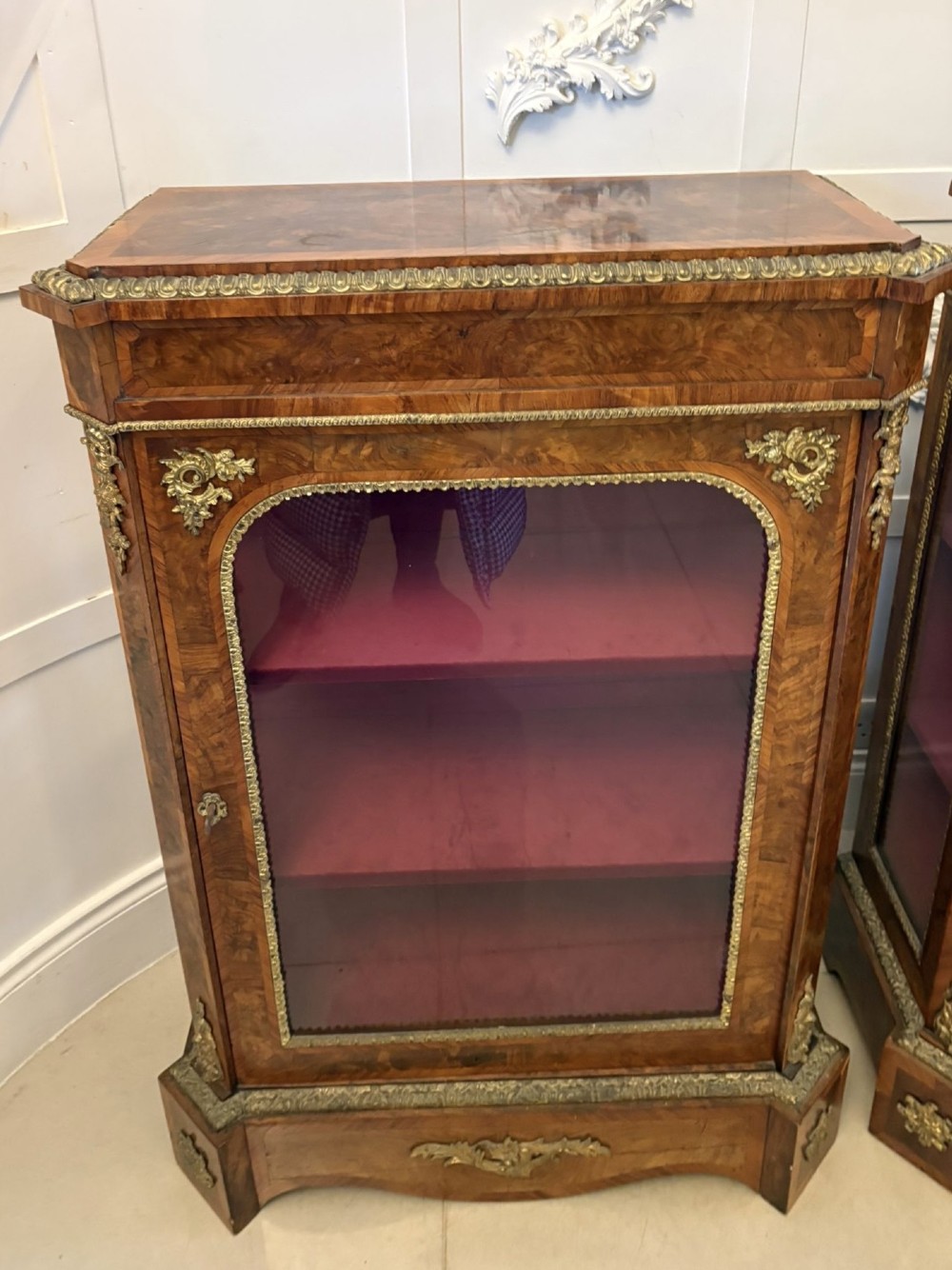 A pair of Victorian burr walnut pier cabinets featuring glazed front doors, velvet-lined interior shelves, and ornate gilt metal mounts. View X
