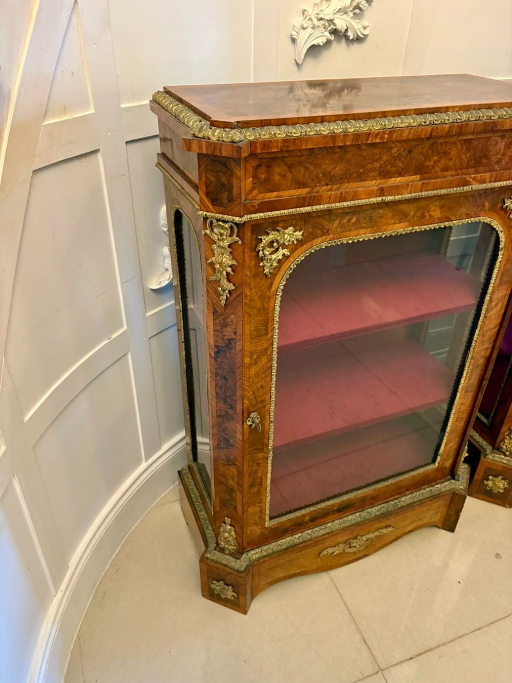 A pair of Victorian burr walnut pier cabinets featuring glazed front doors, velvet-lined interior shelves, and ornate gilt metal mounts. View XI