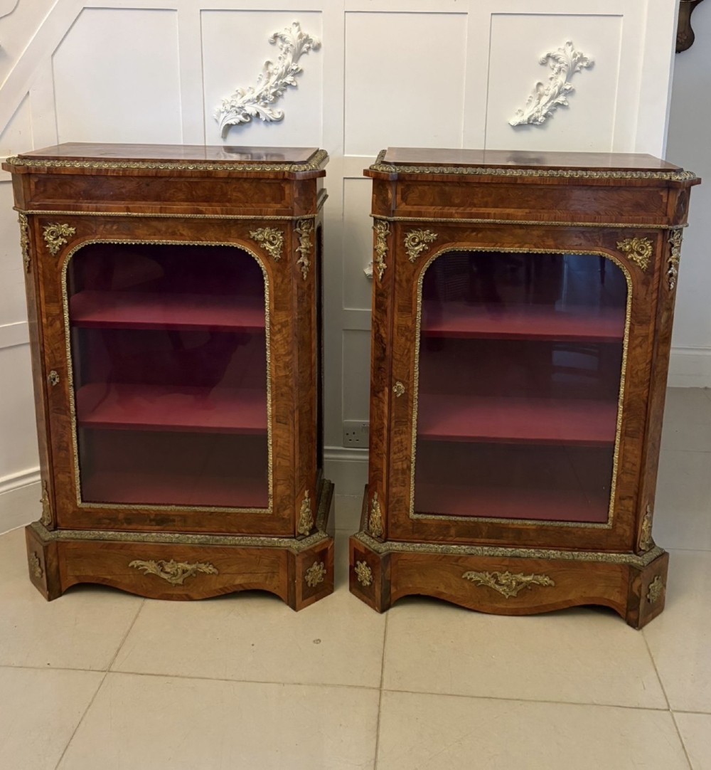 A pair of Victorian burr walnut pier cabinets featuring glazed front doors, velvet-lined interior shelves, and ornate gilt metal mounts. View XII