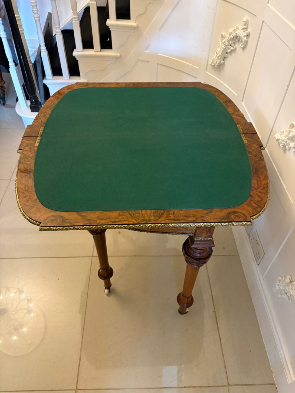 A Victorian burr walnut fold-over card table featuring geometric inlay, turned support legs on castors, and decorative brass edge moulding. View IV