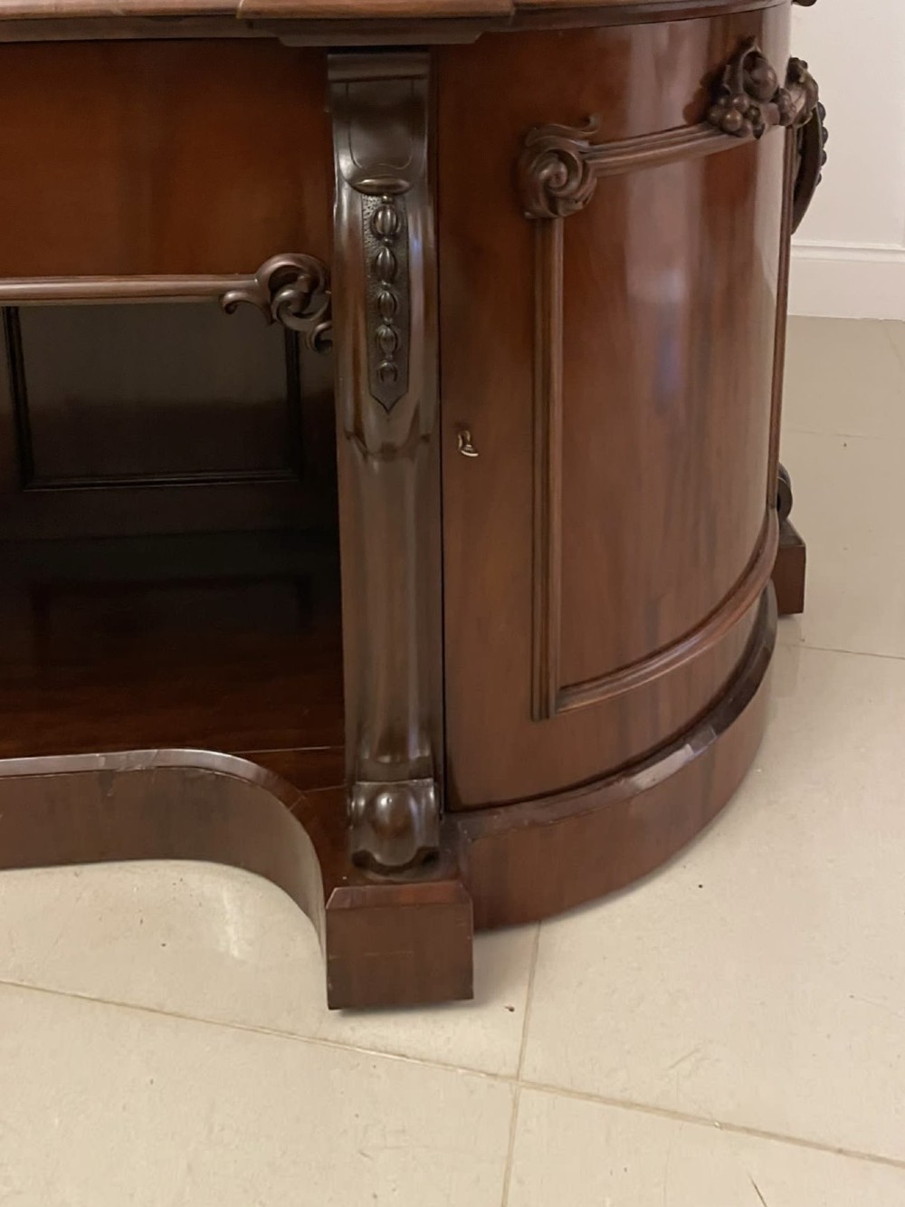 A Victorian carved mahogany sideboard featuring a curved front, open central bay, flanked cupboards, and a large arched mirror backrest adorned with scroll carving. View IX