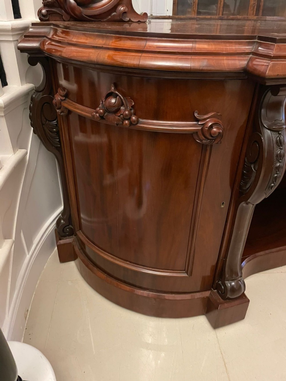 A Victorian carved mahogany sideboard featuring a curved front, open central bay, flanked cupboards, and a large arched mirror backrest adorned with scroll carving. View XI