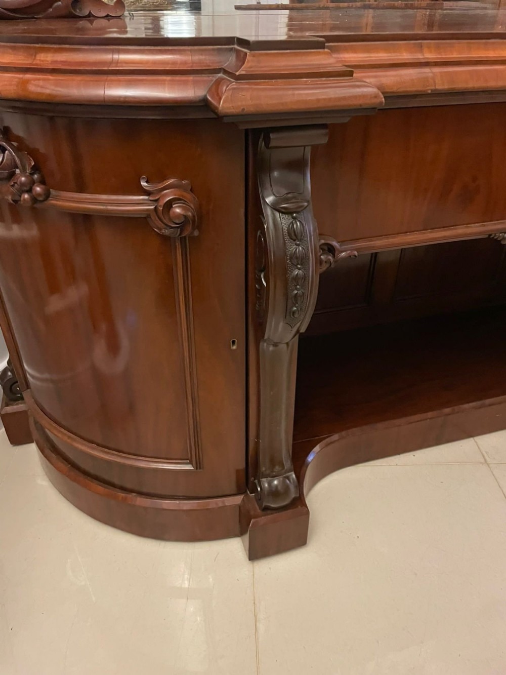 A Victorian carved mahogany sideboard featuring a curved front, open central bay, flanked cupboards, and a large arched mirror backrest adorned with scroll carving. View XII