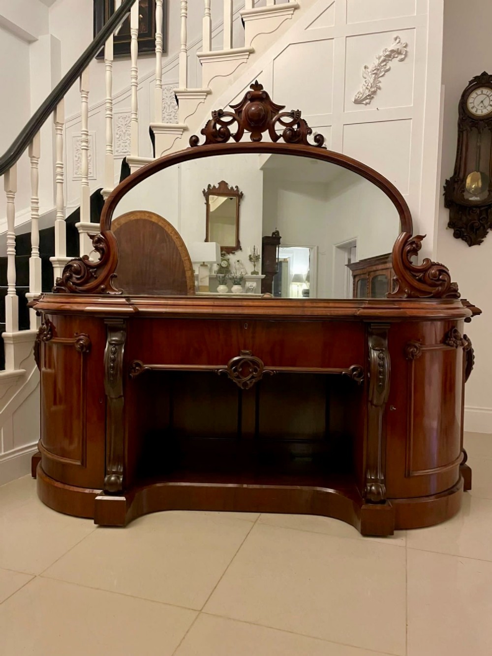 A Victorian carved mahogany sideboard featuring a curved front, open central bay, flanked cupboards, and a large arched mirror backrest adorned with scroll carving. View XIII