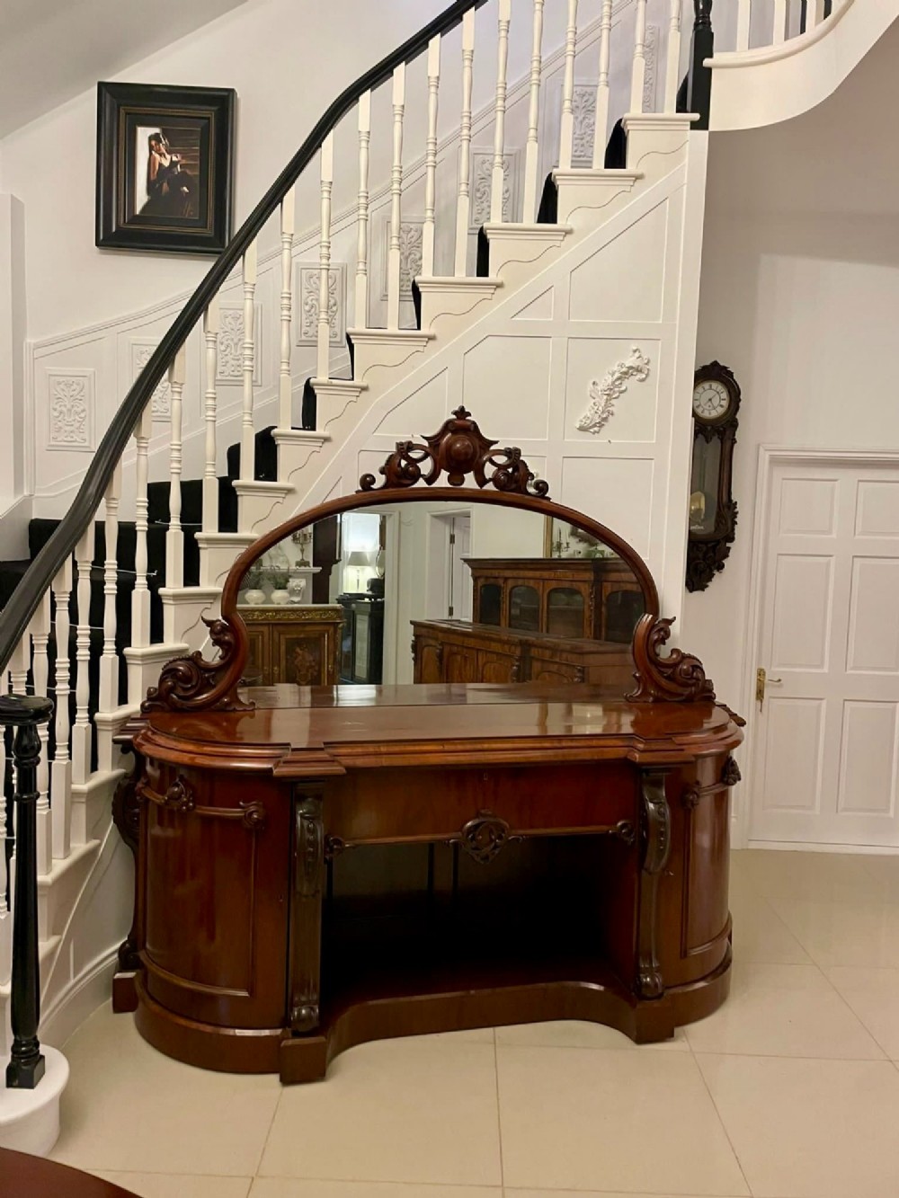 A Victorian carved mahogany sideboard featuring a curved front, open central bay, flanked cupboards, and a large arched mirror backrest adorned with scroll carving.