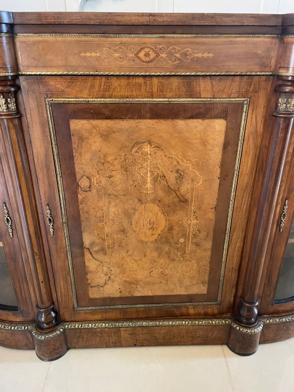 A Victorian burr walnut credenza with a central marquetry inlaid door, gilt ormolu mounts, and two curved glass side display cabinets. View II