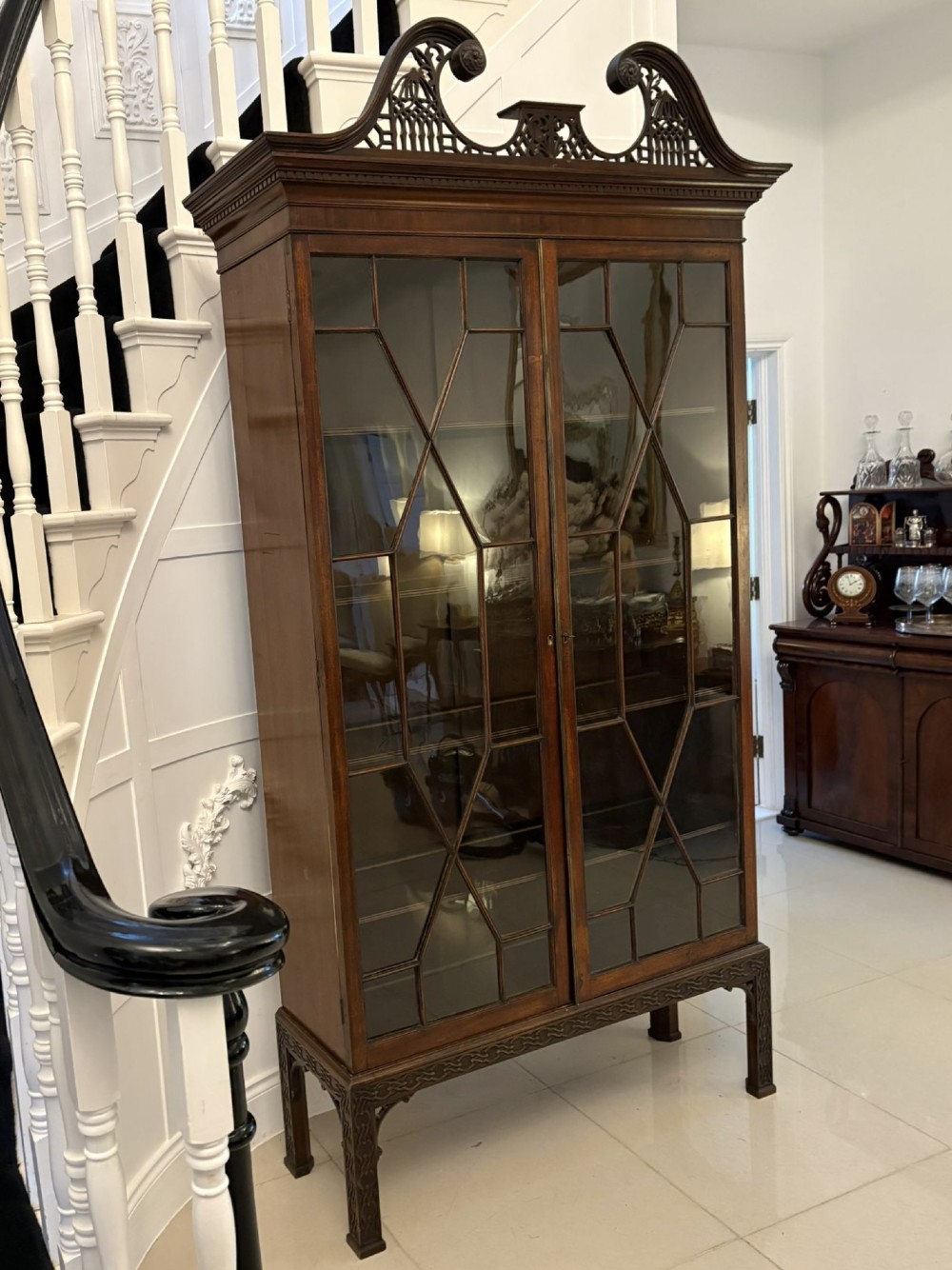 A tall antique Victorian mahogany bookcase featuring a pierced swan-neck pediment, astragal glazed double doors, and carved legs. View II