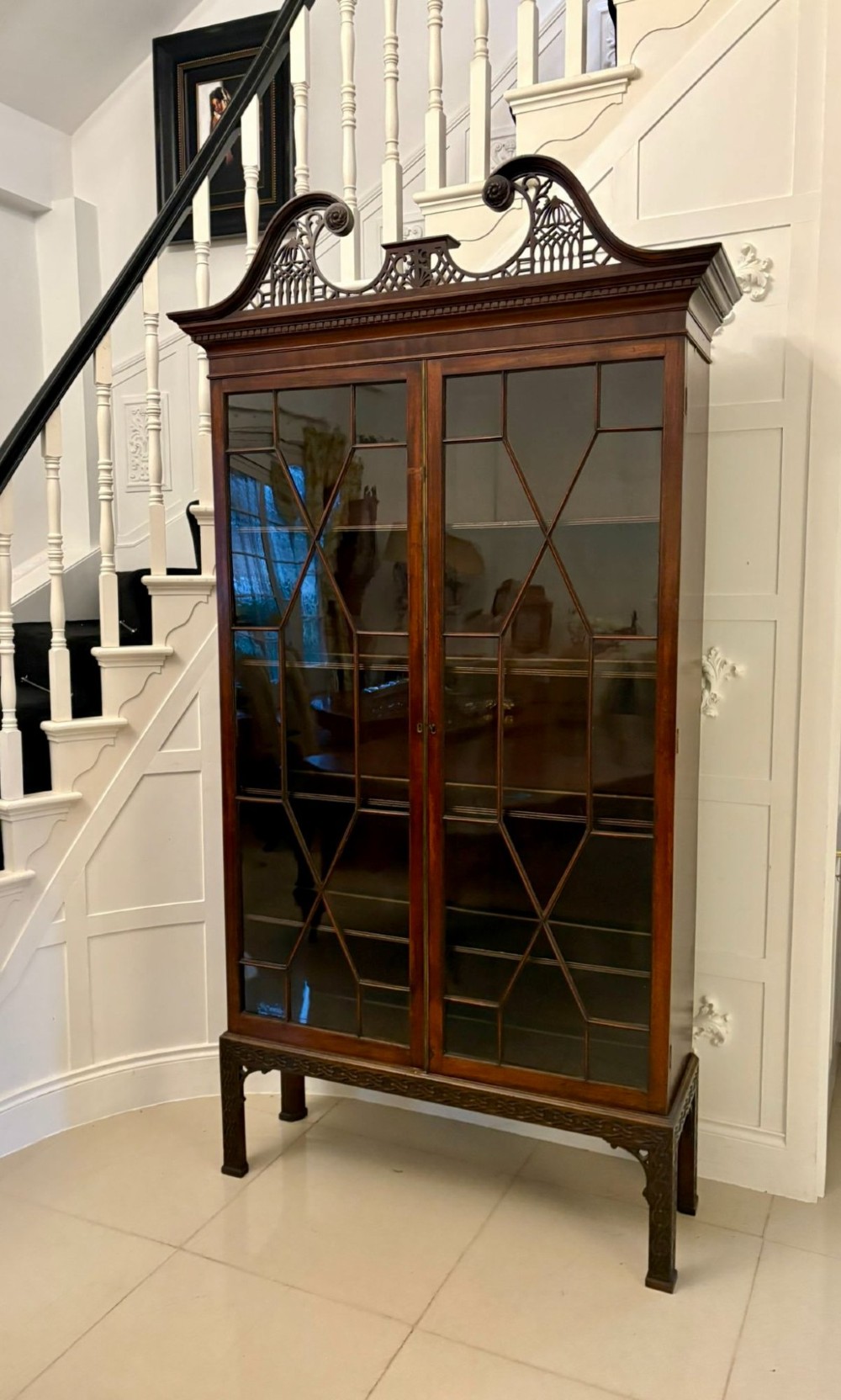 A tall antique Victorian mahogany bookcase featuring a pierced swan-neck pediment, astragal glazed double doors, and carved legs. View VI