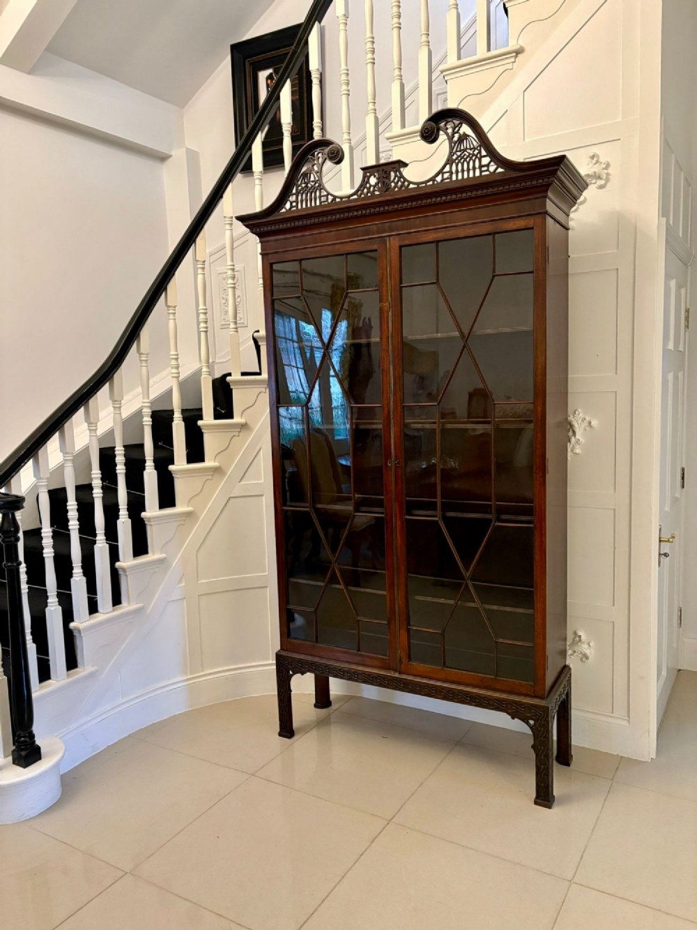 A tall antique Victorian mahogany bookcase featuring a pierced swan-neck pediment, astragal glazed double doors, and carved legs. View VIII