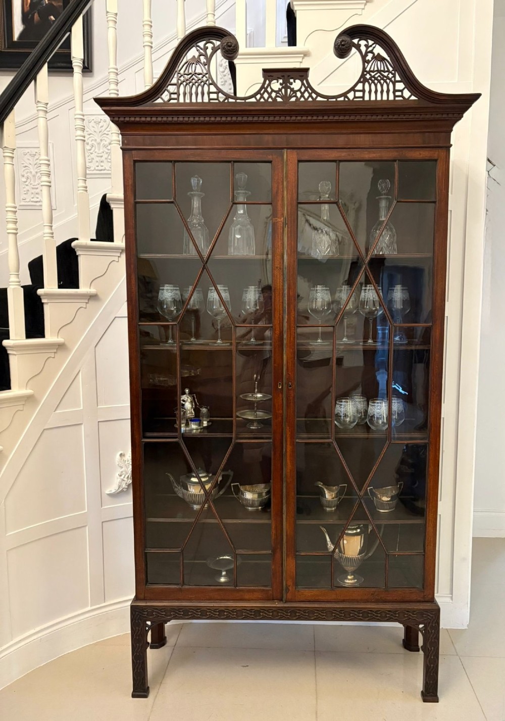 A tall antique Victorian mahogany bookcase featuring a pierced swan-neck pediment, astragal glazed double doors, and carved legs. View IX