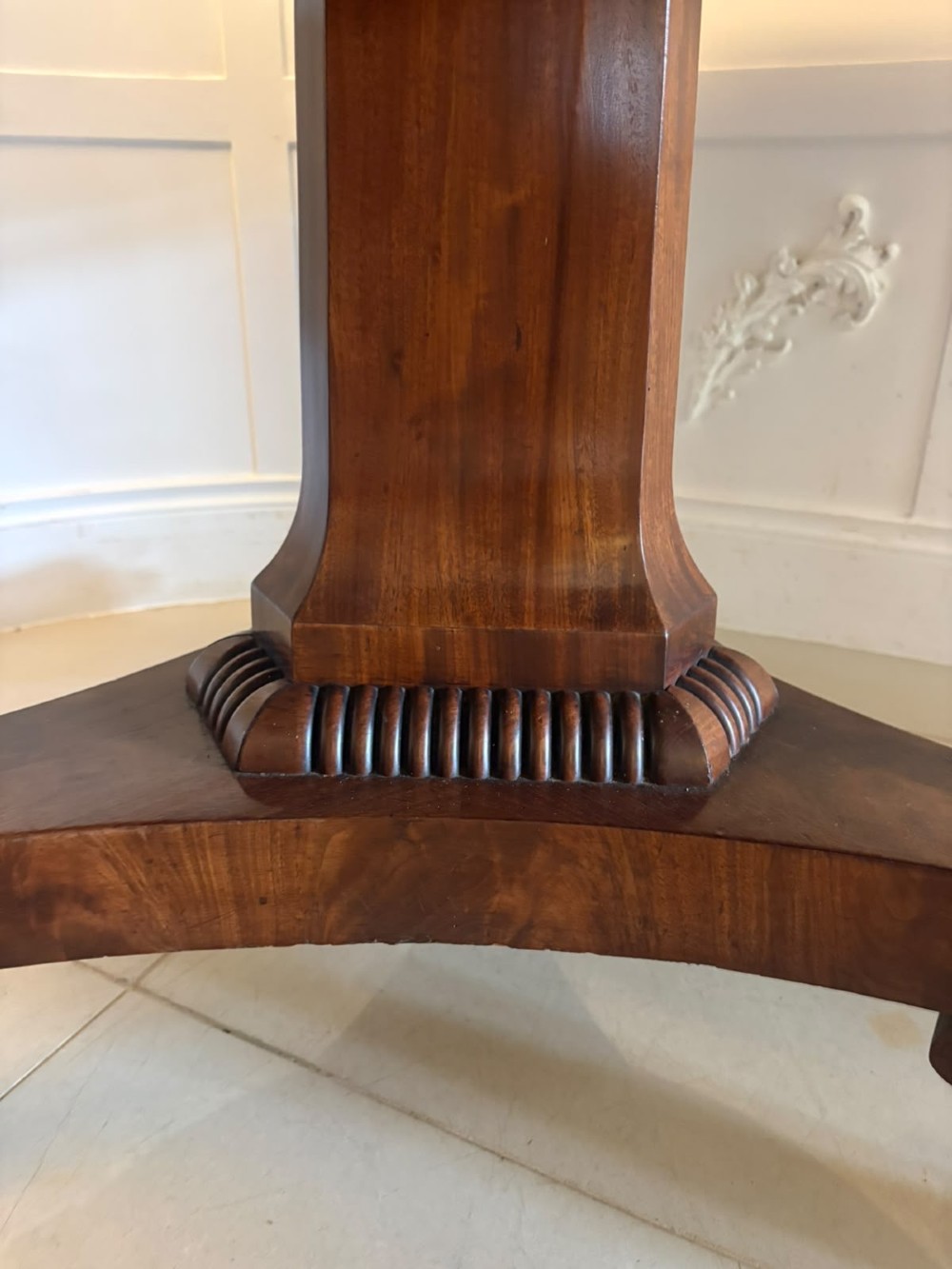 A circular Regency tilt-top centre table featuring highly figured flame mahogany veneers, shown in the upright position on a scrolled pedestal base with brass castors. View IV