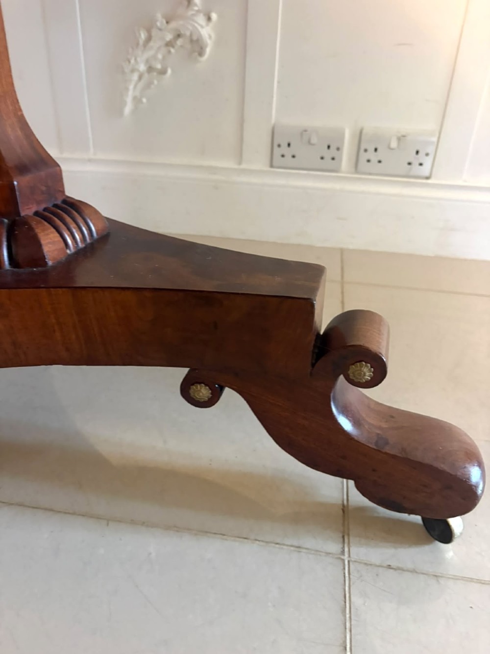 A circular Regency tilt-top centre table featuring highly figured flame mahogany veneers, shown in the upright position on a scrolled pedestal base with brass castors. View VII