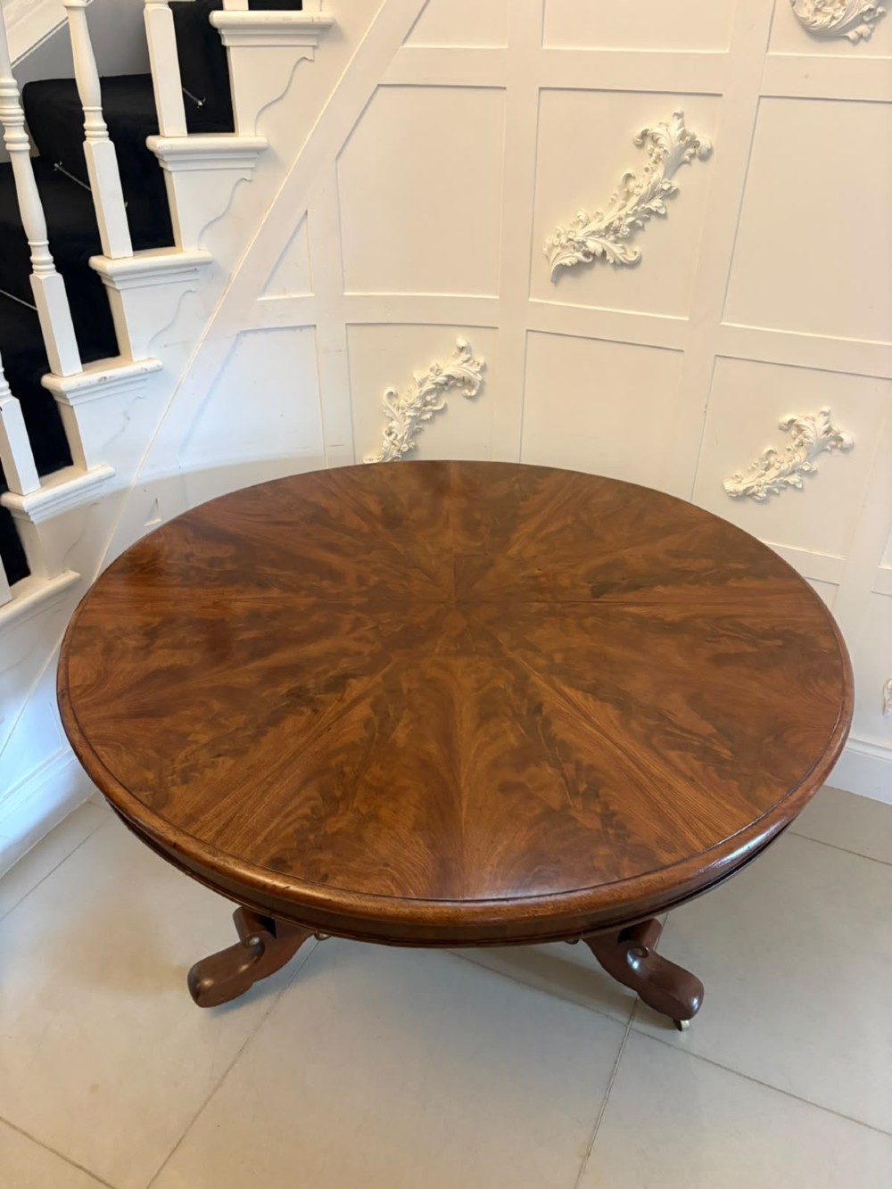 A circular Regency tilt-top centre table featuring highly figured flame mahogany veneers, shown in the upright position on a scrolled pedestal base with brass castors. View IX