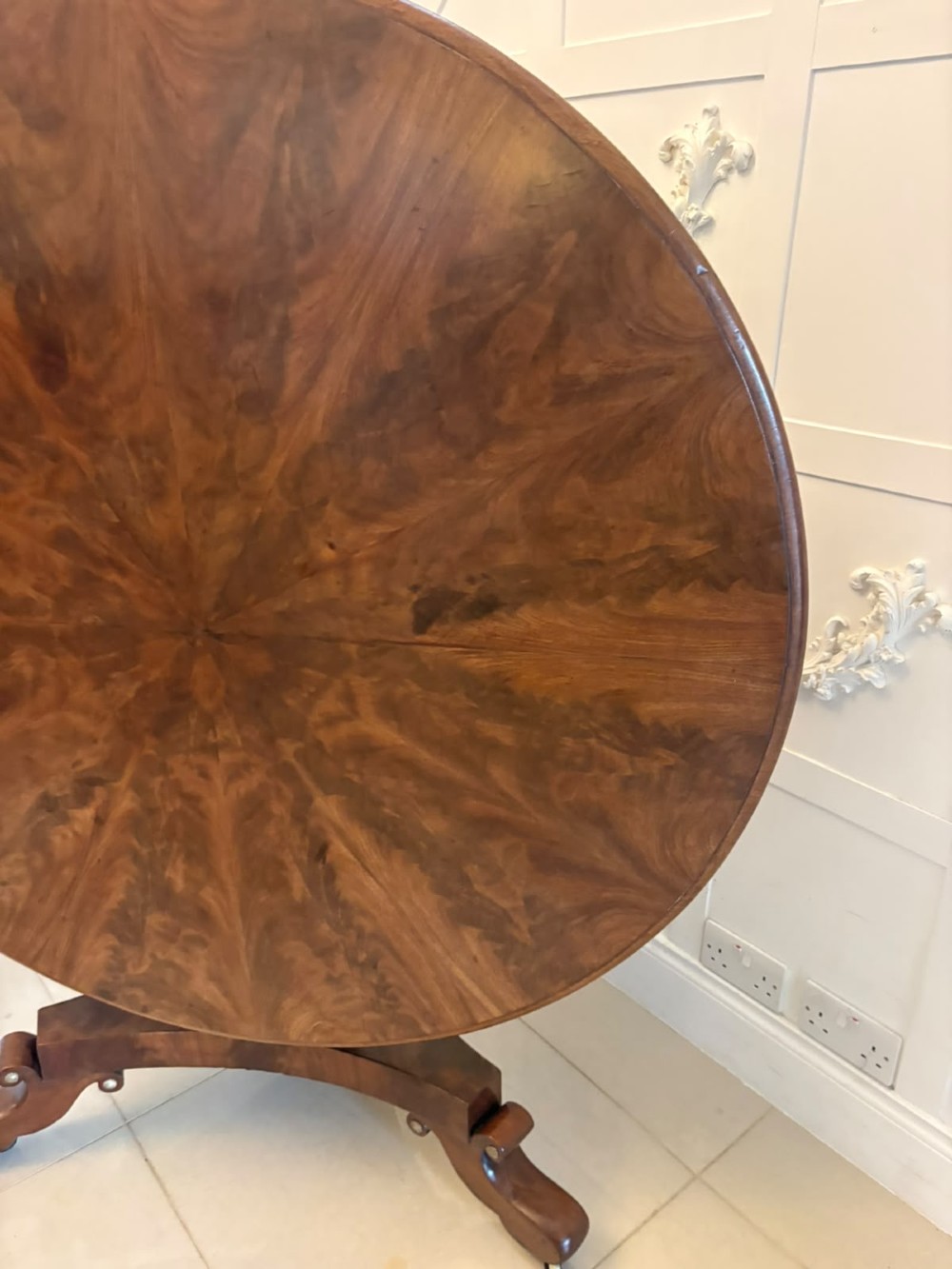 A circular Regency tilt-top centre table featuring highly figured flame mahogany veneers, shown in the upright position on a scrolled pedestal base with brass castors. View XI