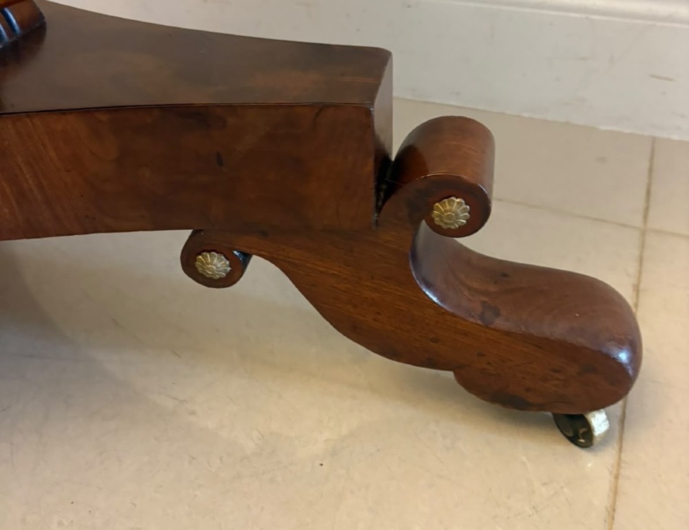 A circular Regency tilt-top centre table featuring highly figured flame mahogany veneers, shown in the upright position on a scrolled pedestal base with brass castors. View XIII