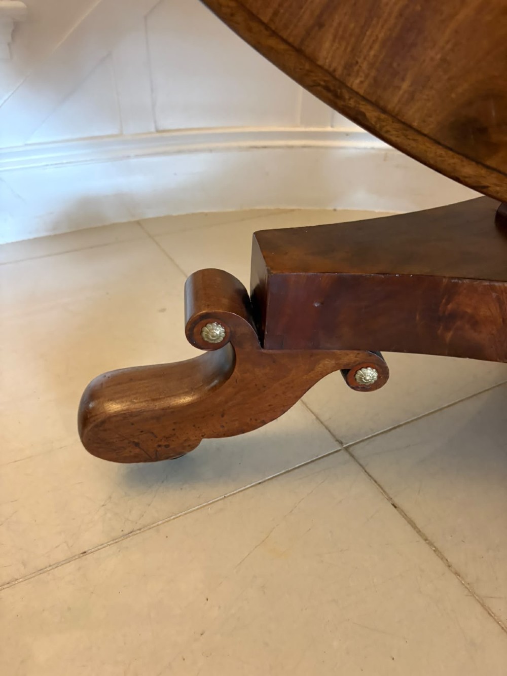 A circular Regency tilt-top centre table featuring highly figured flame mahogany veneers, shown in the upright position on a scrolled pedestal base with brass castors. View XIV