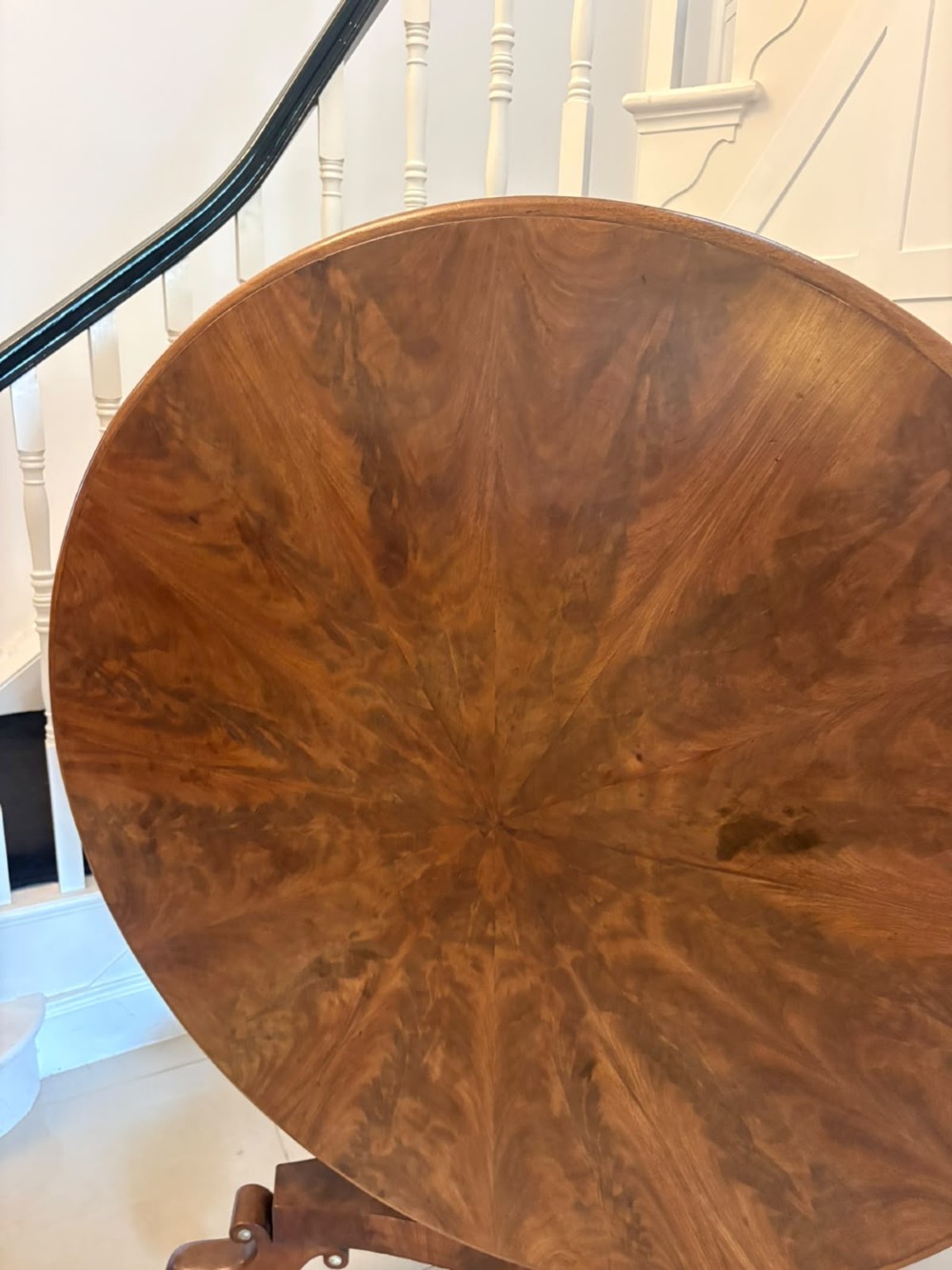 A circular Regency tilt-top centre table featuring highly figured flame mahogany veneers, shown in the upright position on a scrolled pedestal base with brass castors. View XV