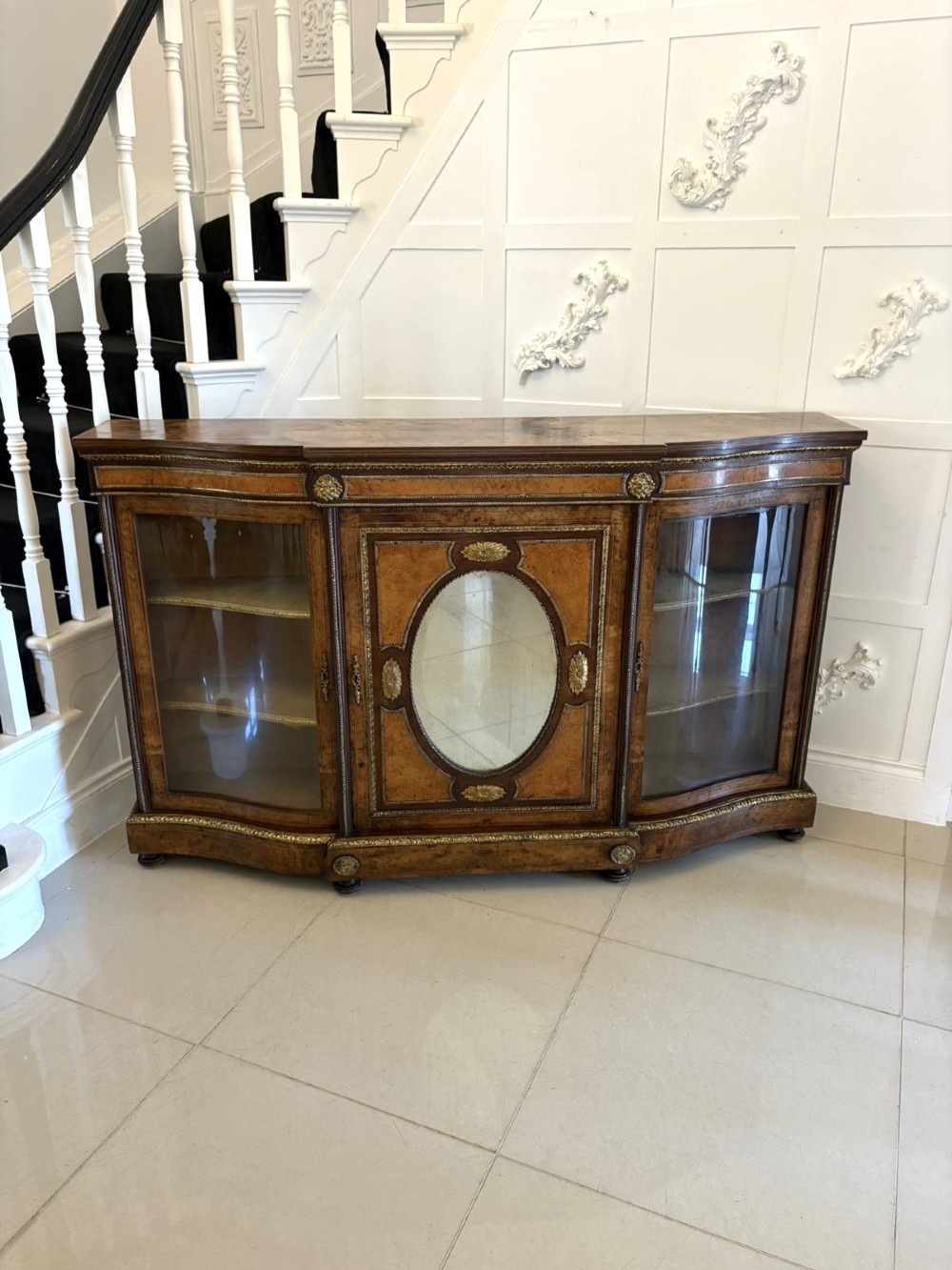 A Victorian burr walnut credenza featuring a central oval mirrored door flanked by curved bow-front glass doors and gilt ormolu mounts.