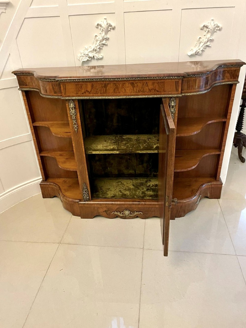 A Victorian burr walnut credenza featuring a central glass door, open serpentine display shelves, and detailed brass ormolu mounts. View IV