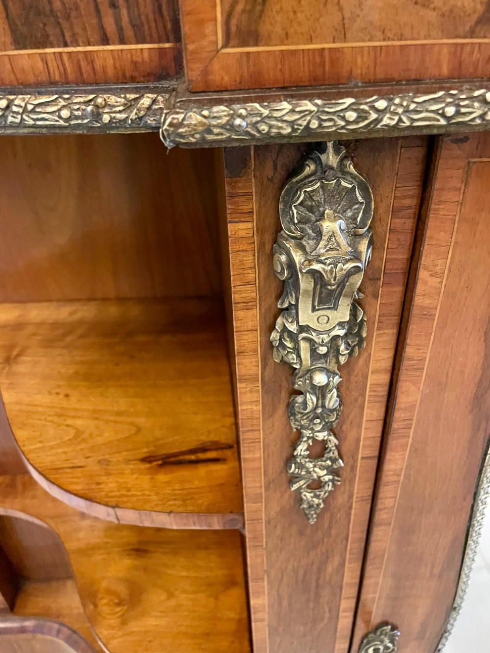 A Victorian burr walnut credenza featuring a central glass door, open serpentine display shelves, and detailed brass ormolu mounts. View X