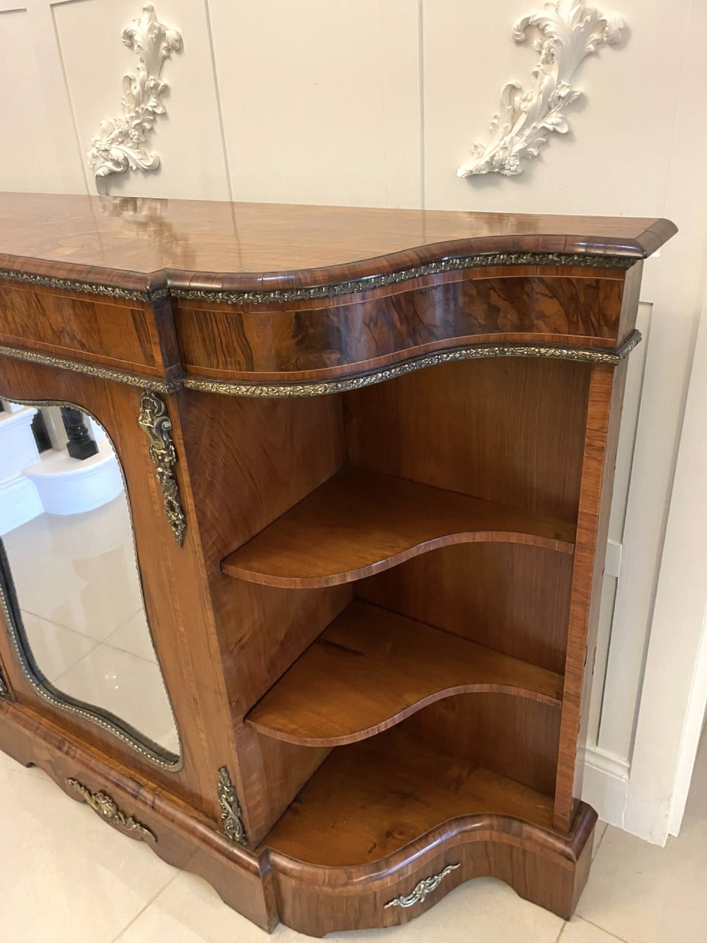 A Victorian burr walnut credenza featuring a central glass door, open serpentine display shelves, and detailed brass ormolu mounts. View XII
