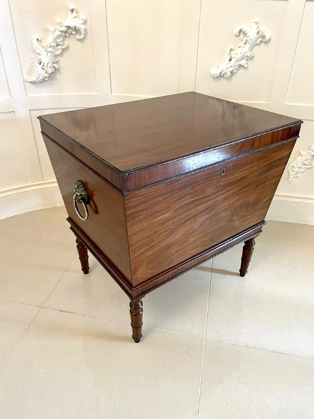 A Georgian mahogany cellarette featuring a tapered rectangular body on turned legs with brass lion-mask side handles and a keyhole lid.