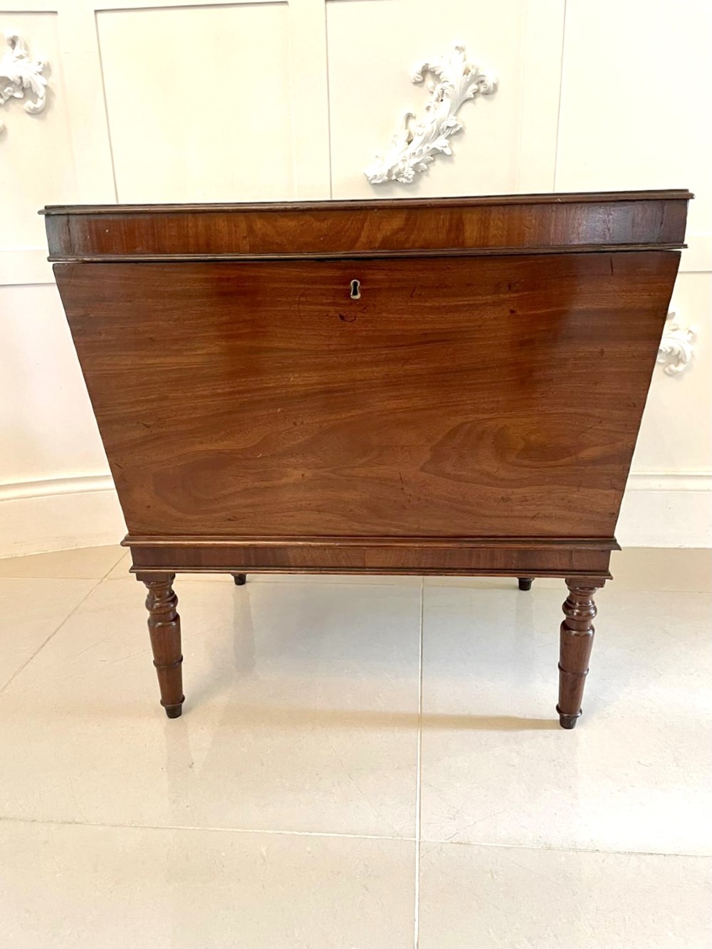 A Georgian mahogany cellarette featuring a tapered rectangular body on turned legs with brass lion-mask side handles and a keyhole lid. View IX