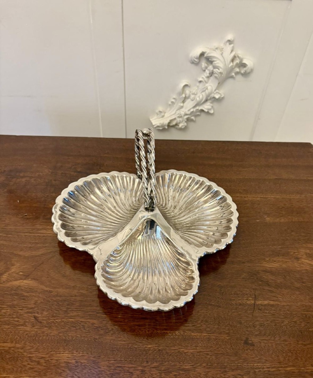 An Edwardian silver-plated tripartite serving dish featuring three fluted shell-shaped compartments joined by a central twisted handle.