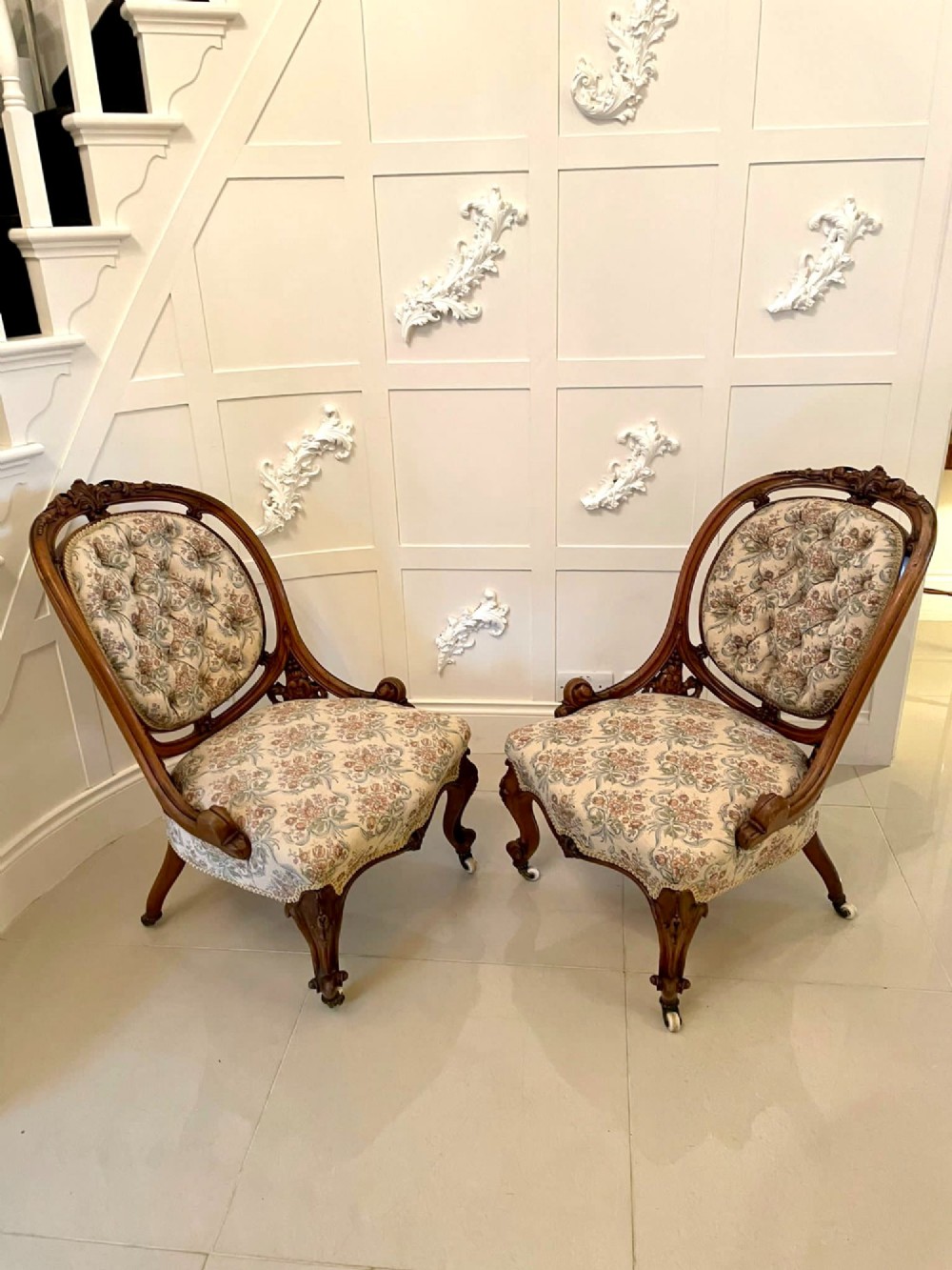 A pair of Victorian carved walnut side chairs featuring button-tufted floral upholstery and cabriole legs with ceramic castors. View VI