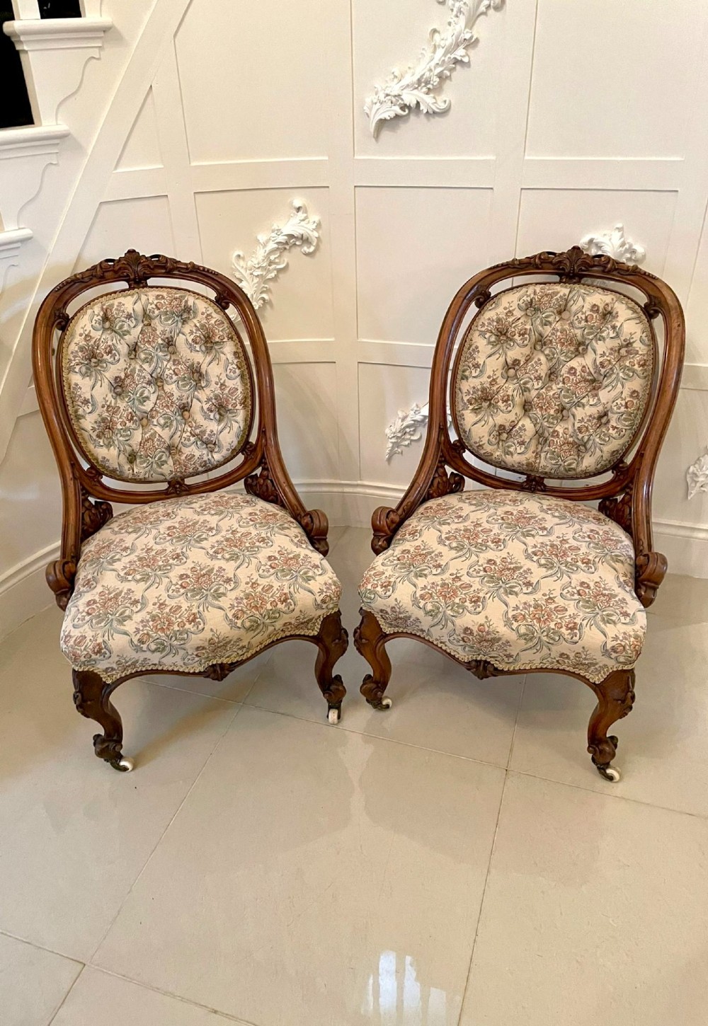A pair of Victorian carved walnut side chairs featuring button-tufted floral upholstery and cabriole legs with ceramic castors.
