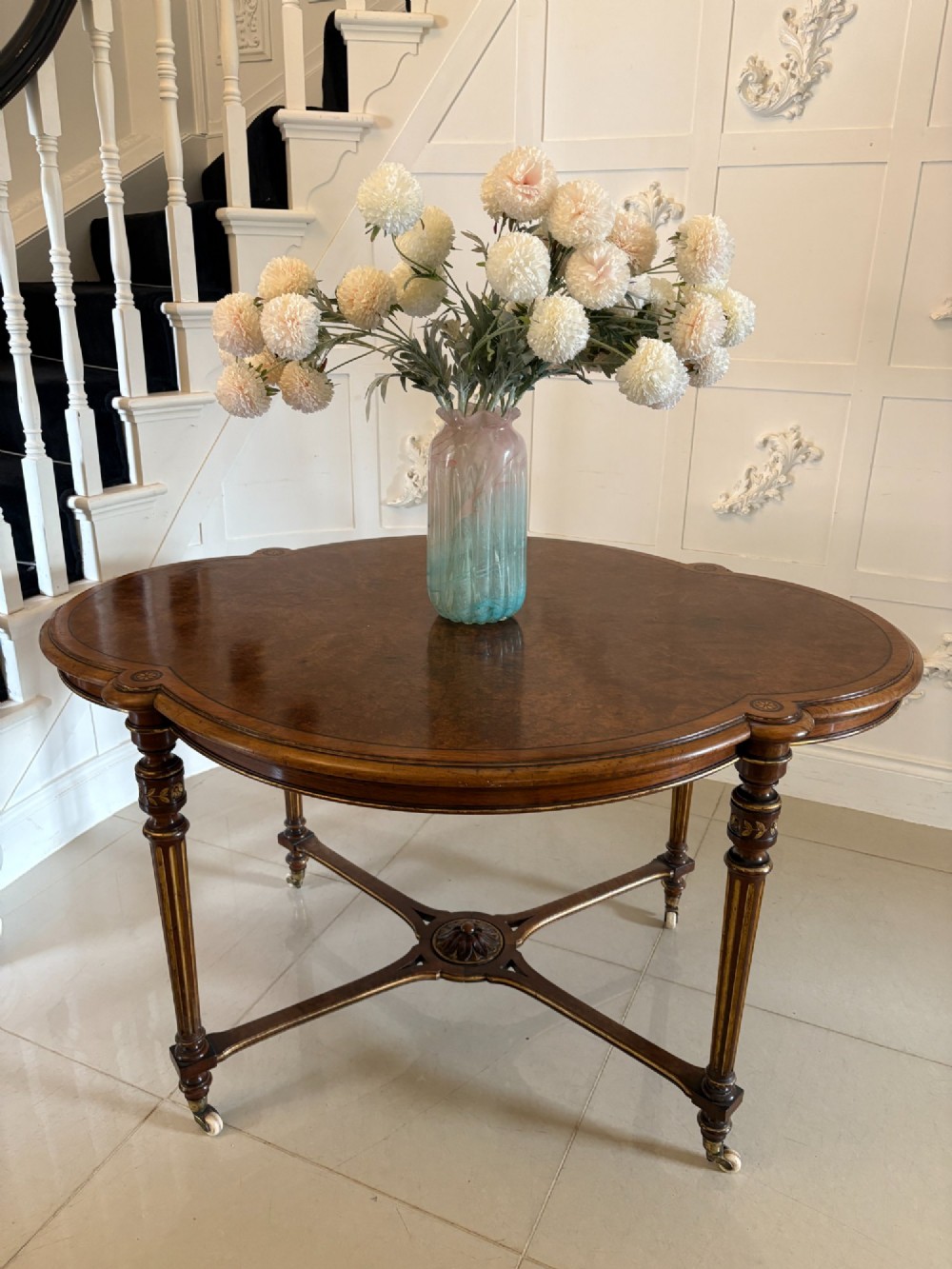 An antique Victorian burr walnut centre table featuring a shaped top with marquetry inlay, turned fluted legs, an X-frame stretcher, and ceramic castors. View II