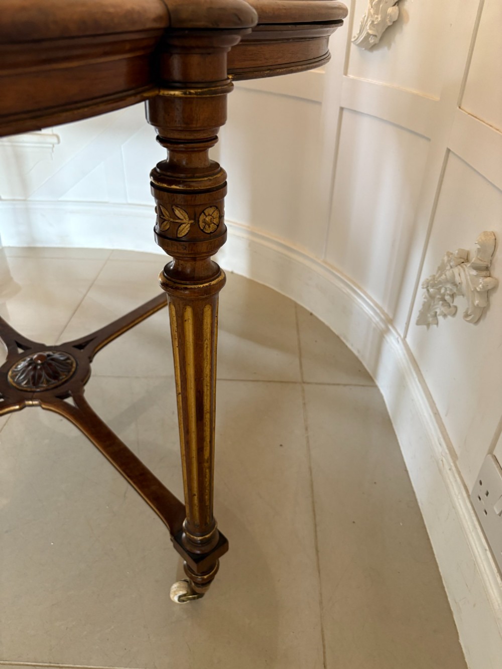 An antique Victorian burr walnut centre table featuring a shaped top with marquetry inlay, turned fluted legs, an X-frame stretcher, and ceramic castors. View IV