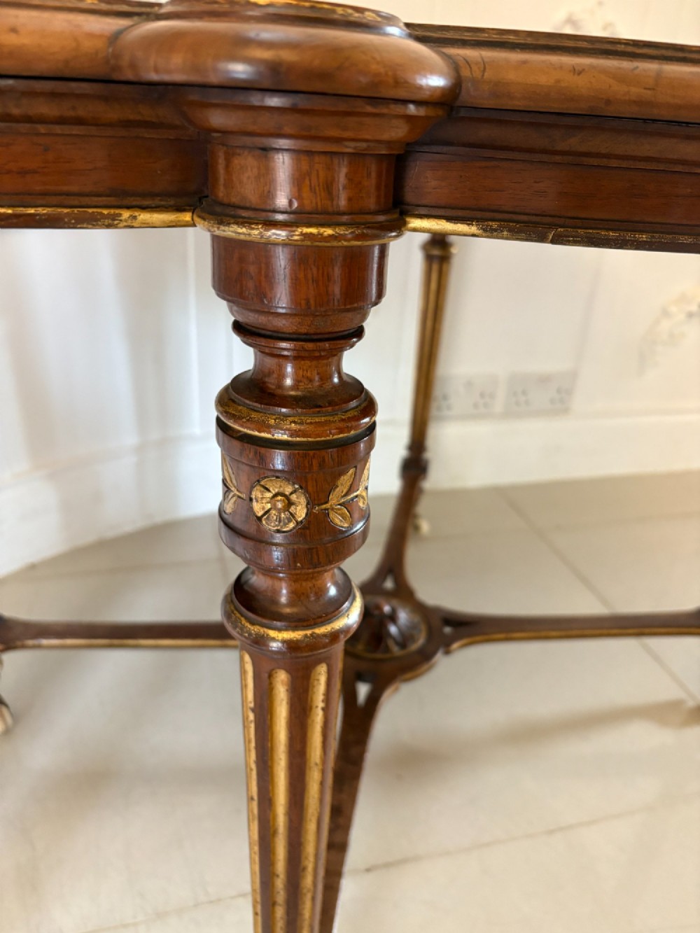 An antique Victorian burr walnut centre table featuring a shaped top with marquetry inlay, turned fluted legs, an X-frame stretcher, and ceramic castors. View IX