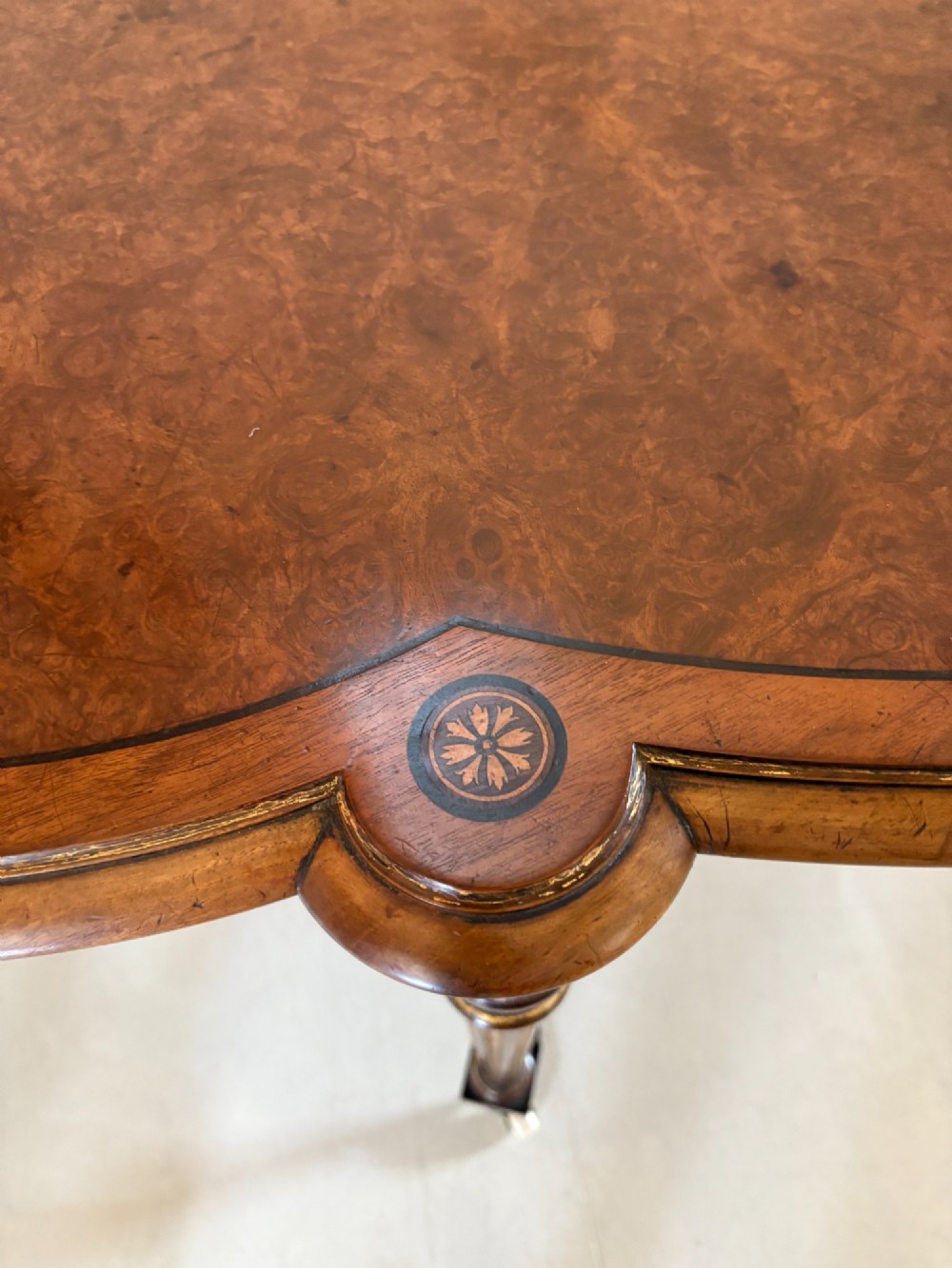An antique Victorian burr walnut centre table featuring a shaped top with marquetry inlay, turned fluted legs, an X-frame stretcher, and ceramic castors. View X