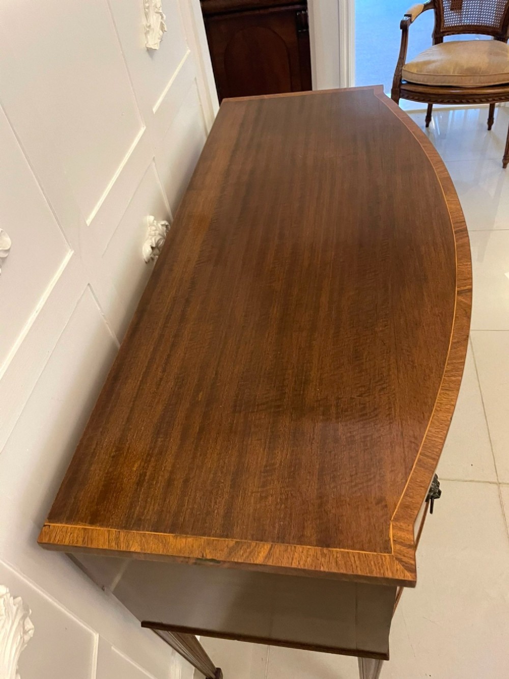An antique bow-fronted mahogany sideboard featuring a central drawer, two side cupboards with oval inlaid panels, brass lion-mask ring handles, and square tapered legs. View II